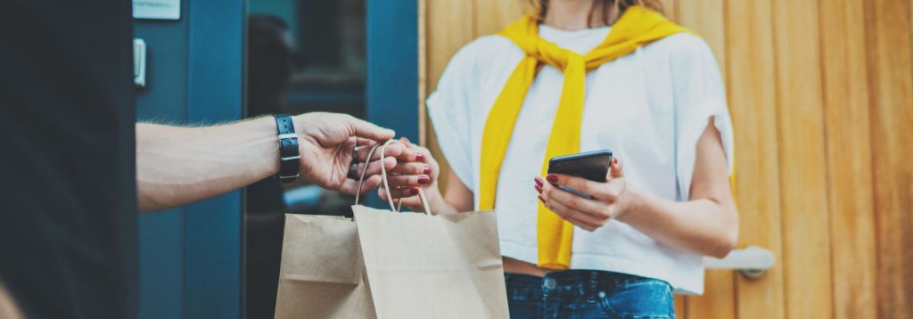 Delivery person handing a bag of food to a woman holding a cellphone