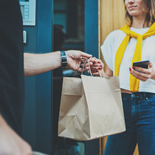 Delivery person handing a bag of food to a woman holding a cellphone